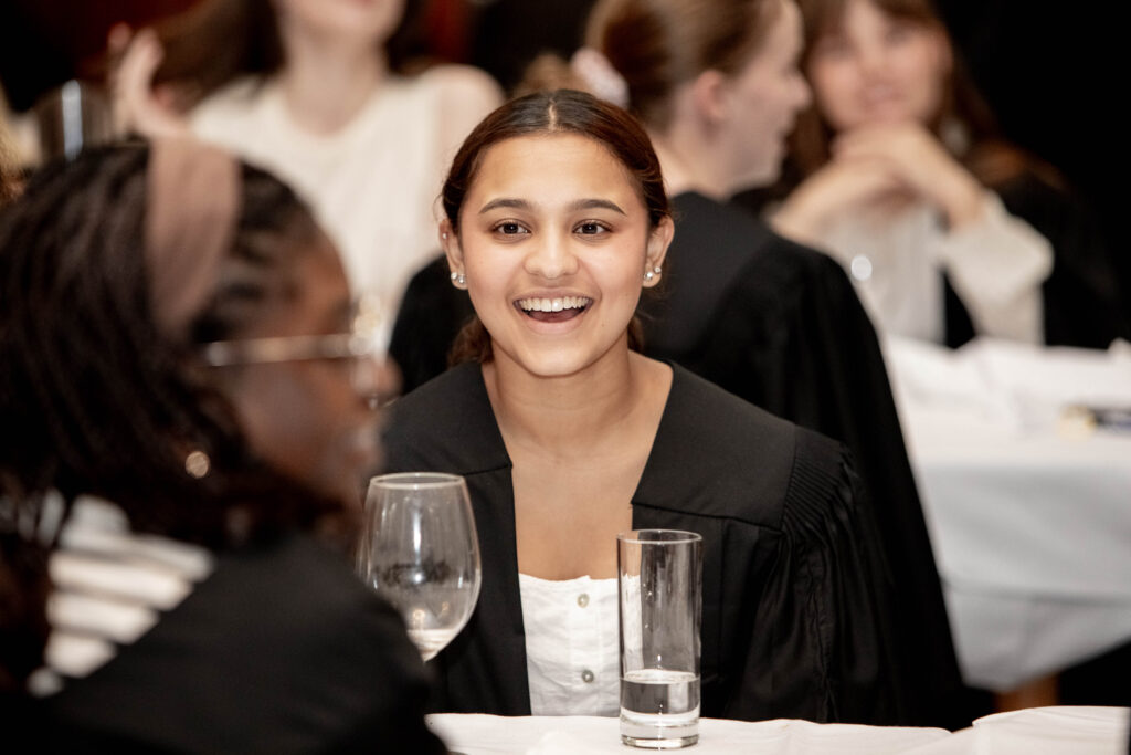 A student at a residential college dinner, wearing an academic gown.