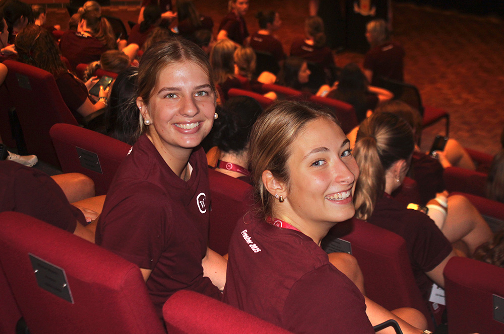Students in uniform sit on chairs at an information session.