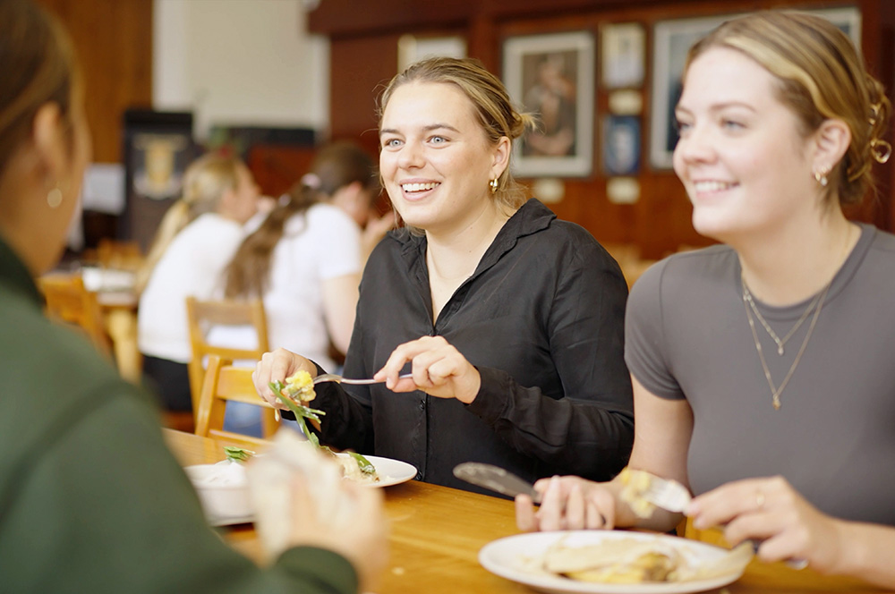 Students eat food in a dining hall at a residential college.